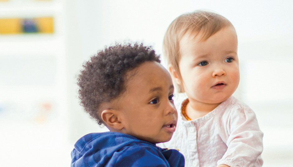 Das Bild zeigt zwei Kleinkinder, ein Mädchen und ein Junge, die Ihren Blick zum rechten Bildrand richten.