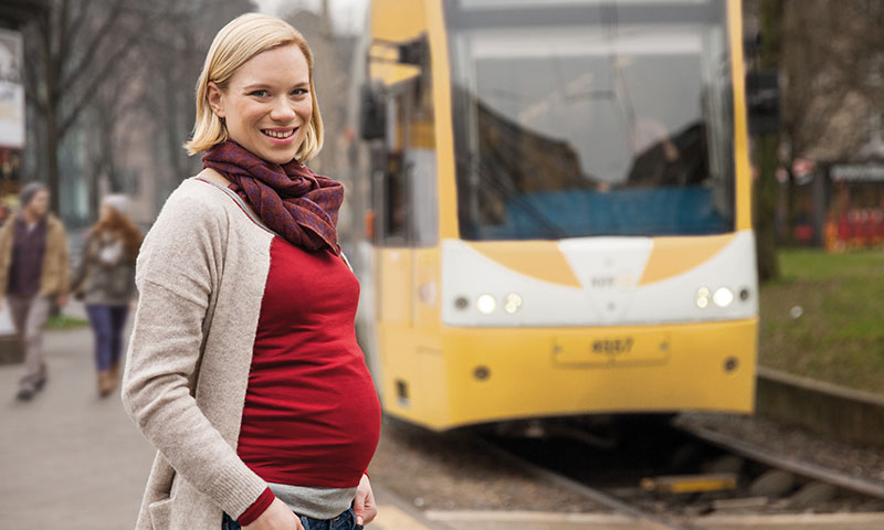 Schwangere Frau steht an einer Straßenbahn